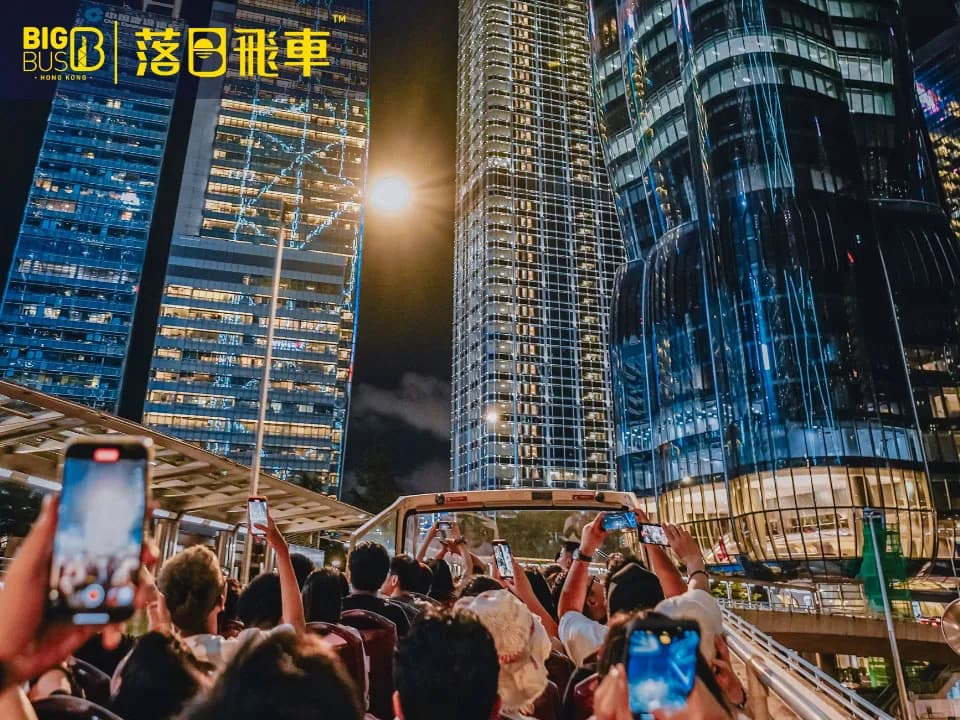 An open-top Big Bus driving through the neon-lit streets of Hong Kong Island at sunset